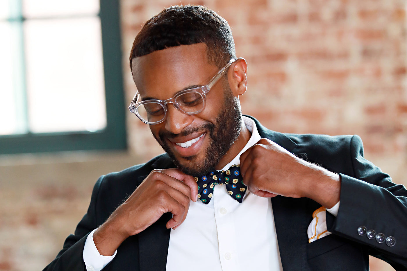 A well-dressed man wearing blue light glasses adjusting his bow tie